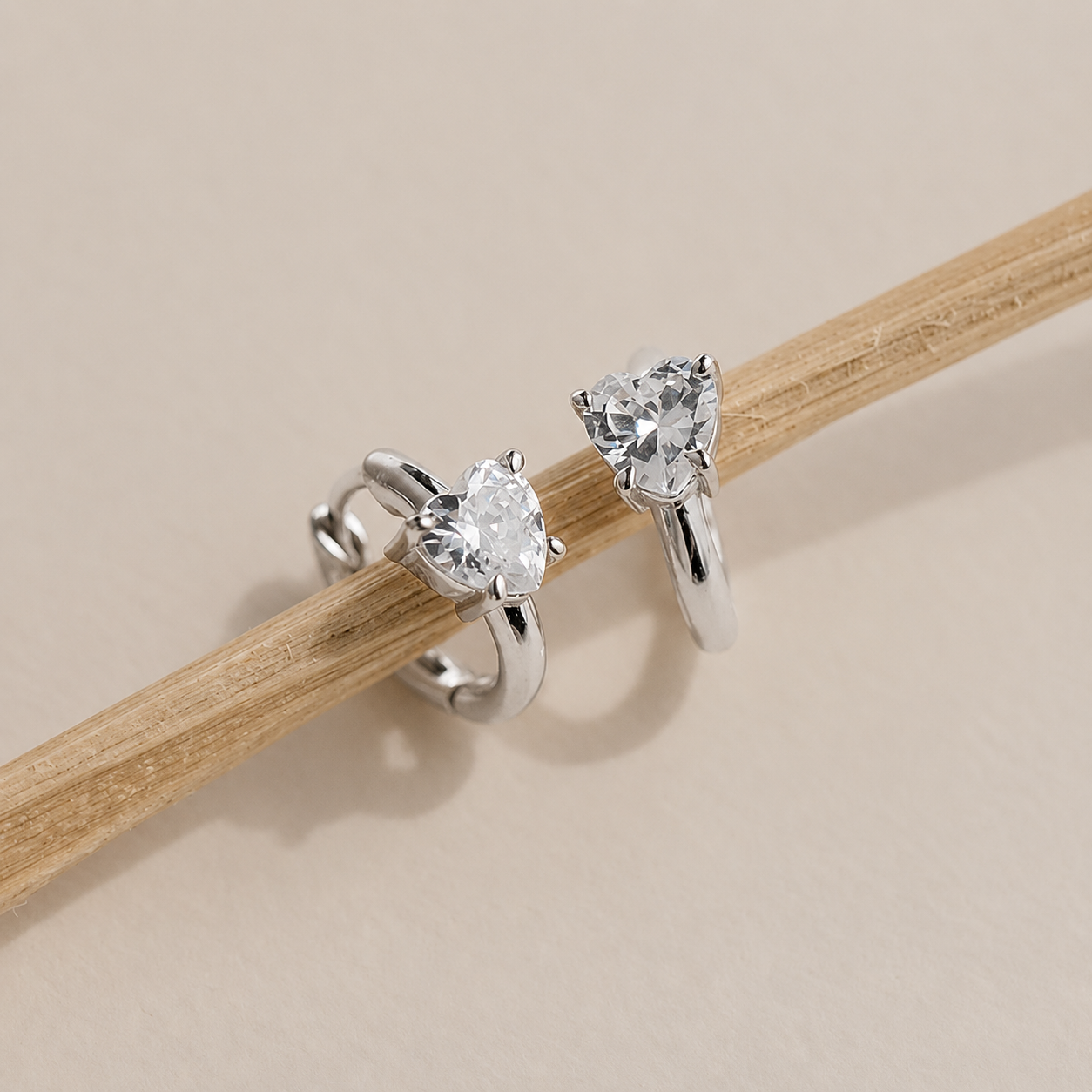 Pair of silver earrings with clear gemstones on a wooden stick against a beige background